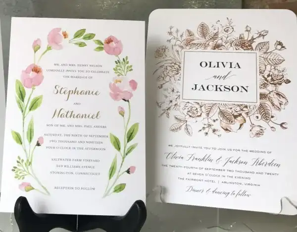 Two custom wedding invitation cards with floral designs on display stands